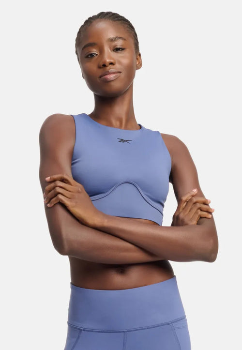 A woman wearing a blue Reebok crop top with a contour panel, designed for fitness activities.