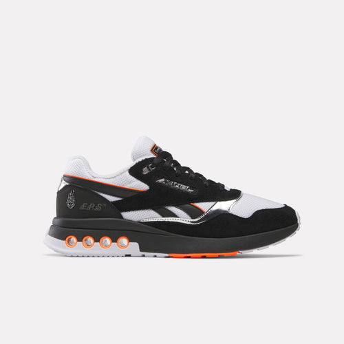 Black and white sneaker with orange accents Reebok x Anuel AA ERS World Sneaker on a light gray background